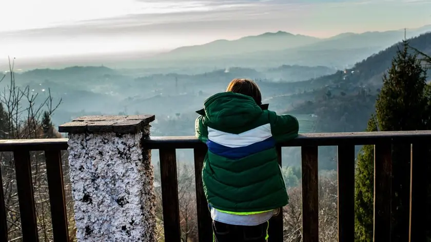 Boy looking out at mountain valley landscape from balcony, rear view, Piani Resinelli, Lombardy, Italy