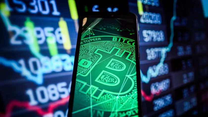 Logo Bitcoin visualizzato su uno smartphone con le percentuali del mercato azionario sullo sfondo.