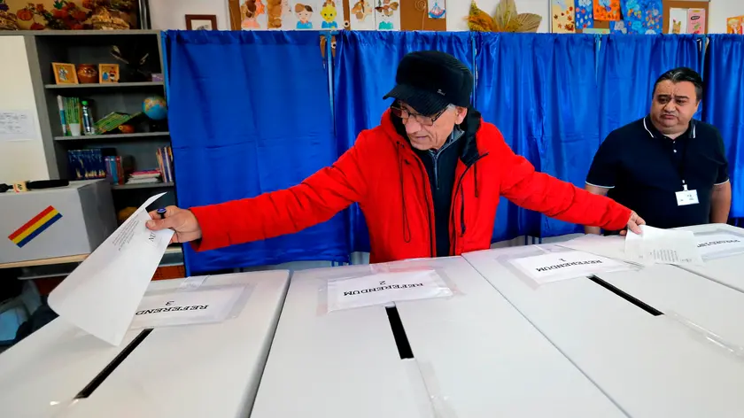 epa11738389 An elderly man stretches to cast his ballot for the first round of presidential elections under the scrutiny of a volunteer man (R), at a polling station in Bucharest, Romania, 24 November 2024. Marcel Ciolacu, leader of the Social Democratic Party (PSD) and incumbent prime minister, still leads in the presidential race according to the latest vote intention surveys, followed by Alliance for the Union of Romanians (AUR) leader George Simion, and Save Romania Union (USR) candidate Elena Lasconi. Romanians vote today for ninth presidential election, with a second round planned for 08 December 2024. Approximately 18 million Romanian citizens are expected at the polling stations this weekend, according to the Permanent Electoral Authority (AEP), of which 989,230 people can express their intention abroad. EPA/BOGDAN CRISTEL