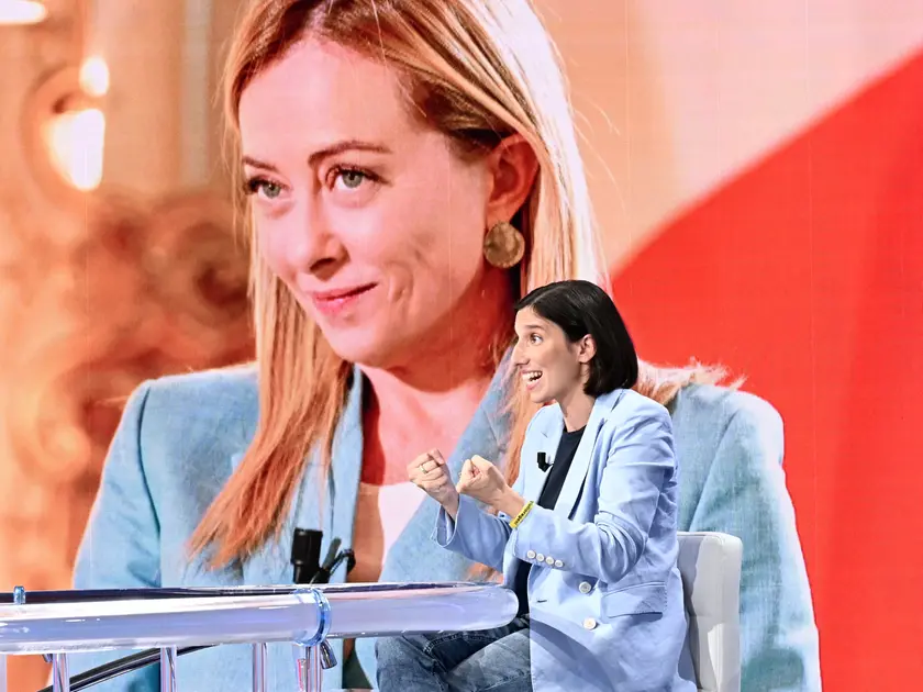 Nella foto Elly Schlein, sullo sfondo un’immagine della Meloni