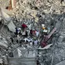 Palestinesi cercano tra le macerie degli edifici distrutti dopo un attacco aereo israeliano