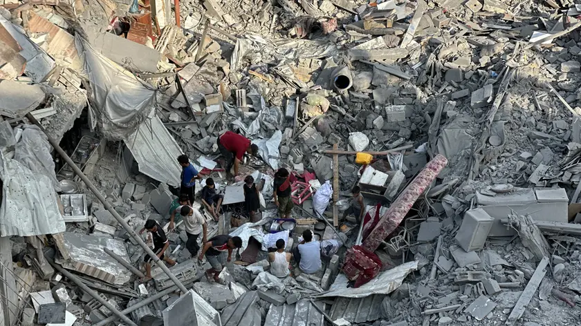 Palestinesi cercano tra le macerie degli edifici distrutti dopo un attacco aereo israeliano