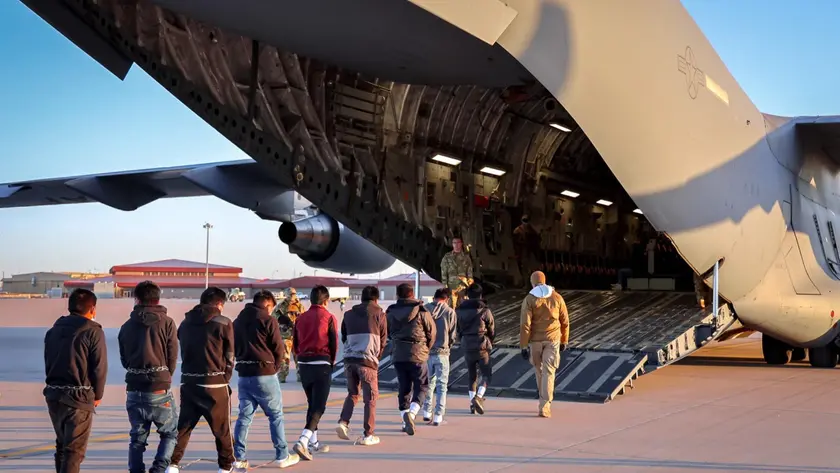 La fila di migranti mentre vengono imbarcati su un aereo militare Usa