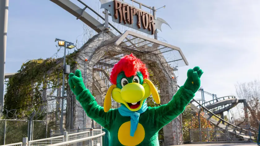 Prezzemolo, la mascotte di Gardaland, davanti a Raptor, una delle attrazioni simbolo del parco
