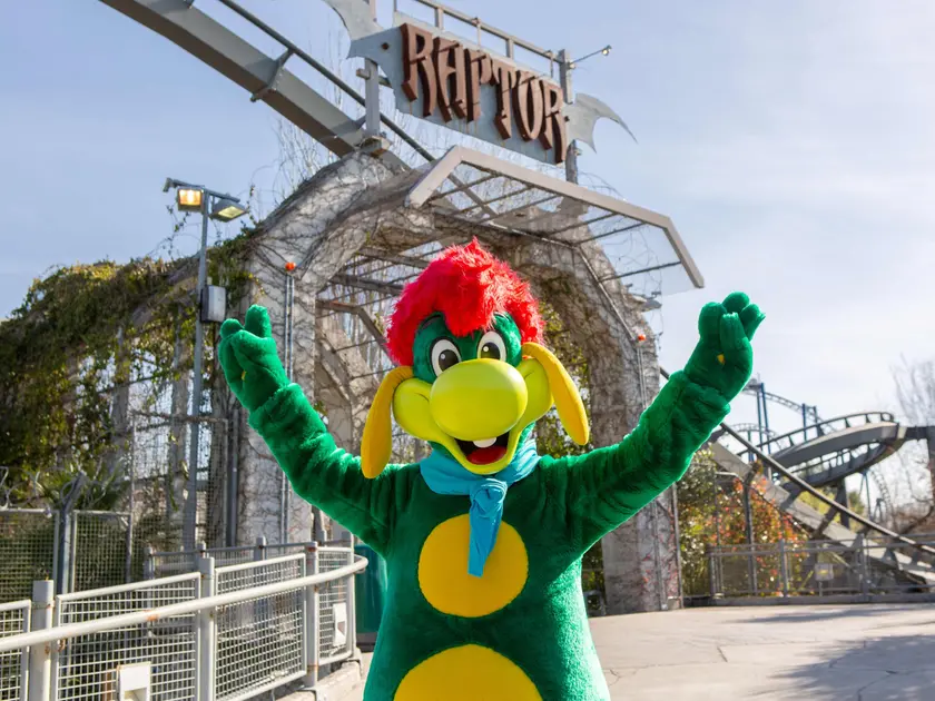 Prezzemolo, la mascotte di Gardaland, davanti a Raptor, una delle attrazioni simbolo del parco