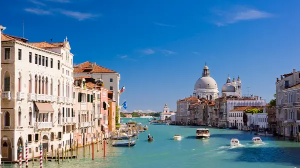 The Grand Canal and Santa Maria della Salute church in Venice, Italy. Boats moving on the river under a clear blue summer sky.