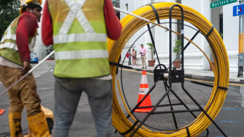 Singapore, Republic of Singapore, Asia - Two workers are laying cables on a road in the central business district.