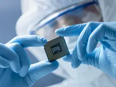 In Ultra Modern Electronic Manufacturing Factory Design Engineer in Sterile Coverall Holds Microchip with Gloves and Examines it.