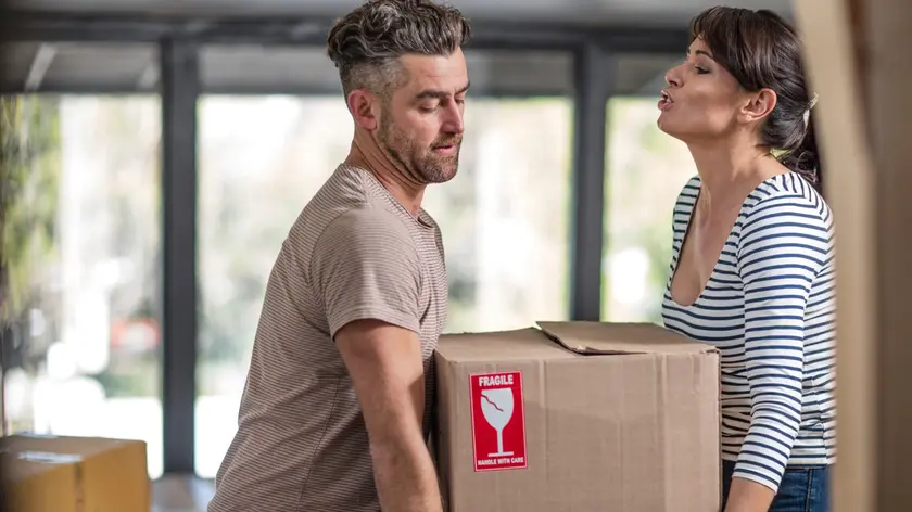 Couple in unfurnished home, carrying box of fragile belongings