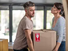 Couple in unfurnished home, carrying box of fragile belongings