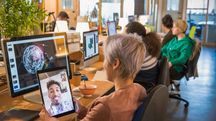 Creative businesswoman video chatting with businessman on digital tablet in open plan office