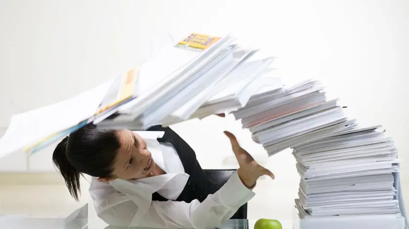 A woman in an office with a large pile of paper.