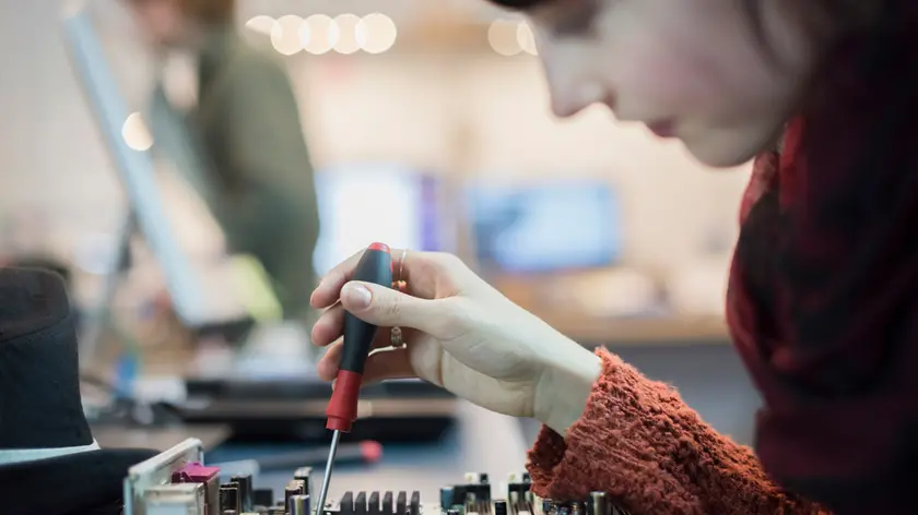 Computer Repair Shop. A woman using an electronic screwdriver tool on a computer circuit board.