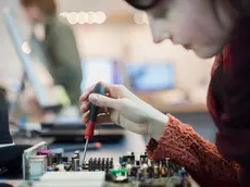 Computer Repair Shop. A woman using an electronic screwdriver tool on a computer circuit board.