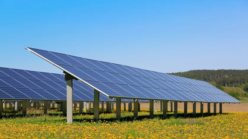 Solar panels on an open green field with yellow flowers and blue sky in the spring. Salo, Finland.